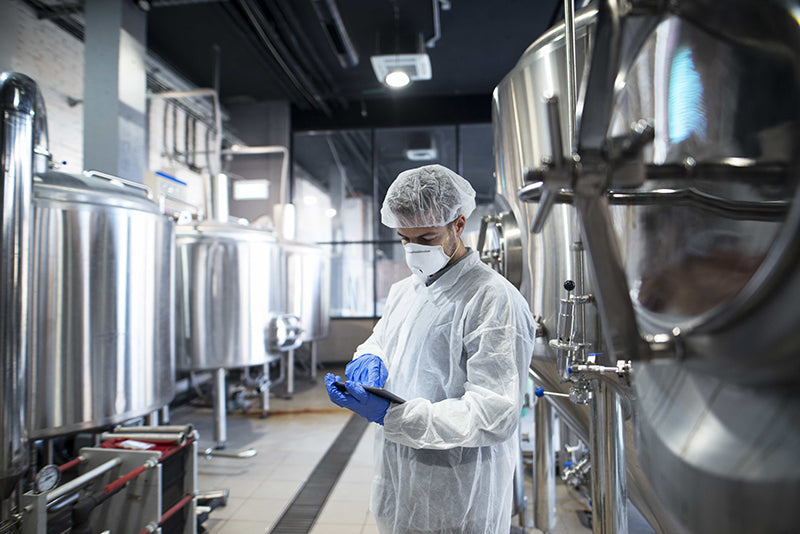 Scientist in cleanroom suit inspecting bioprocessing equipment in a GMP-compliant pharmaceutical manufacturing facility.