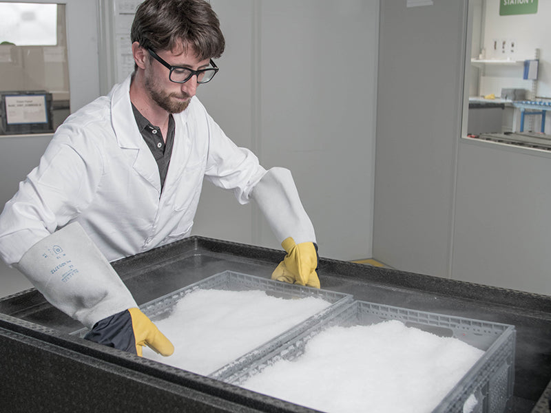 Person with lab coat and gloves preparing frozen drug substance shipment using RoSS.SHIP cold chain container.