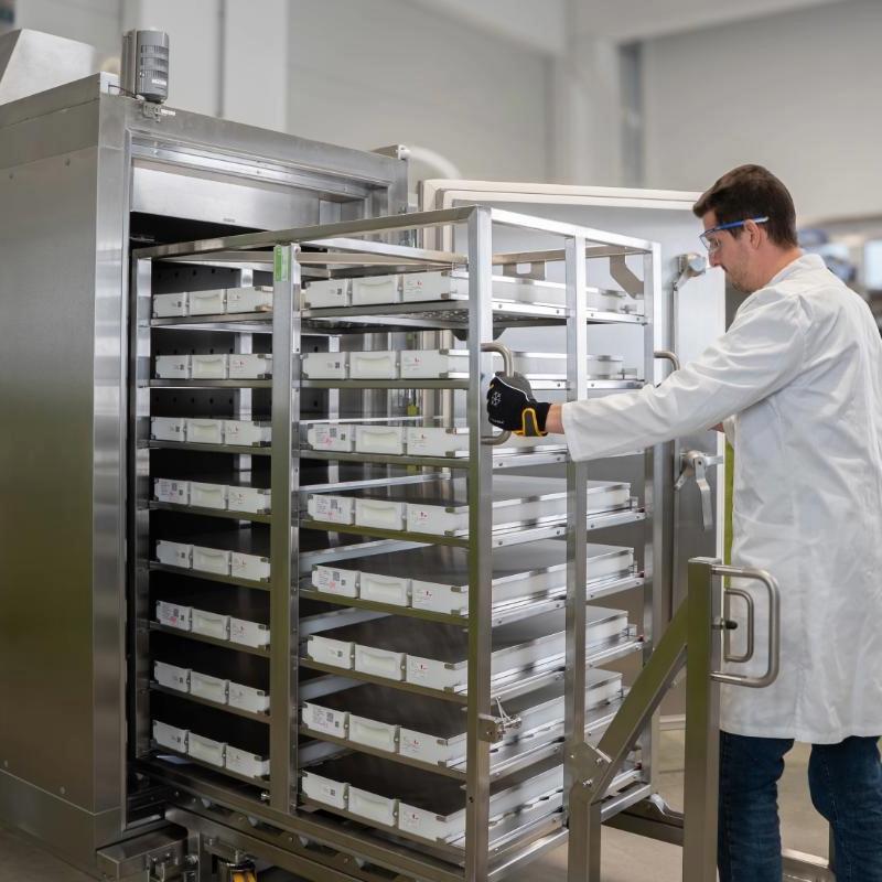 Manufacturing operator in a lab coat working with a large industrial blast freezer with a batch of drug substance in single-use bioprocess containers.