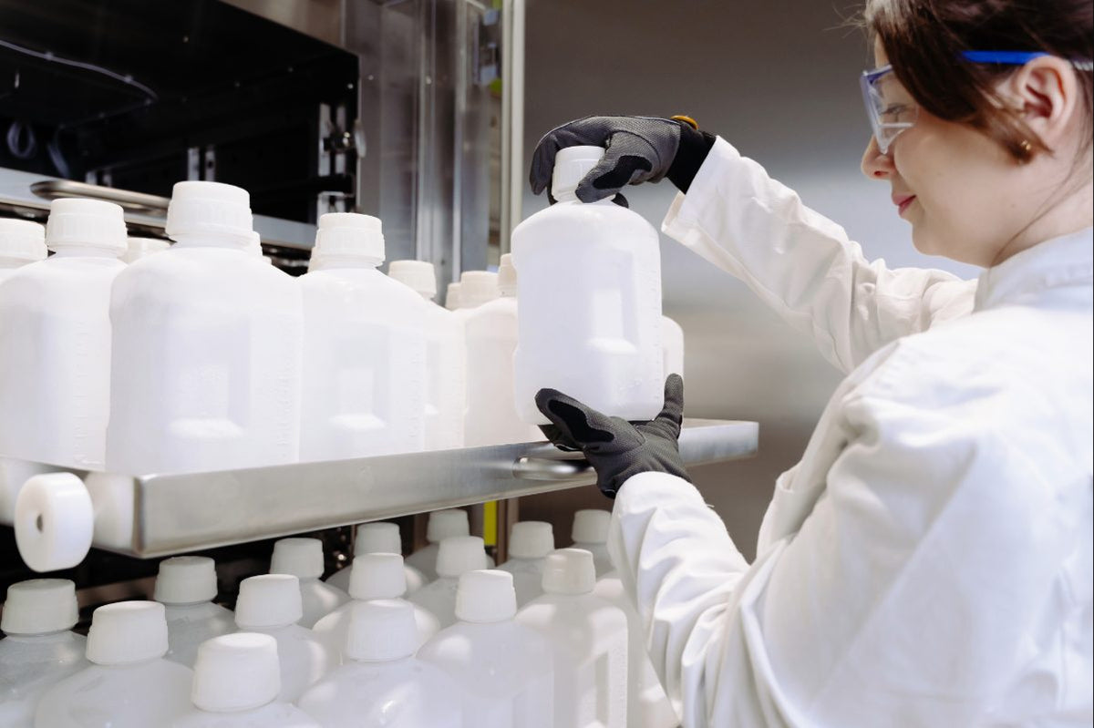 Biomanufacturing operator handling frozen bioprocess containers, wearing protective gear in front of controlled blast freezer.
