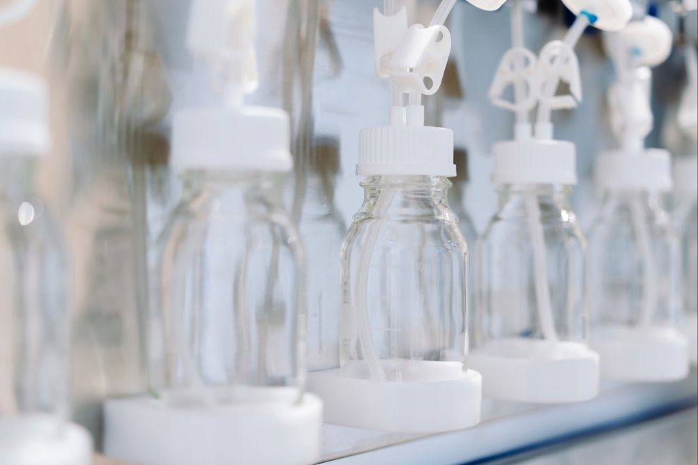 Biomanufacturing setup with PETG bottles and white caps on a filling module.