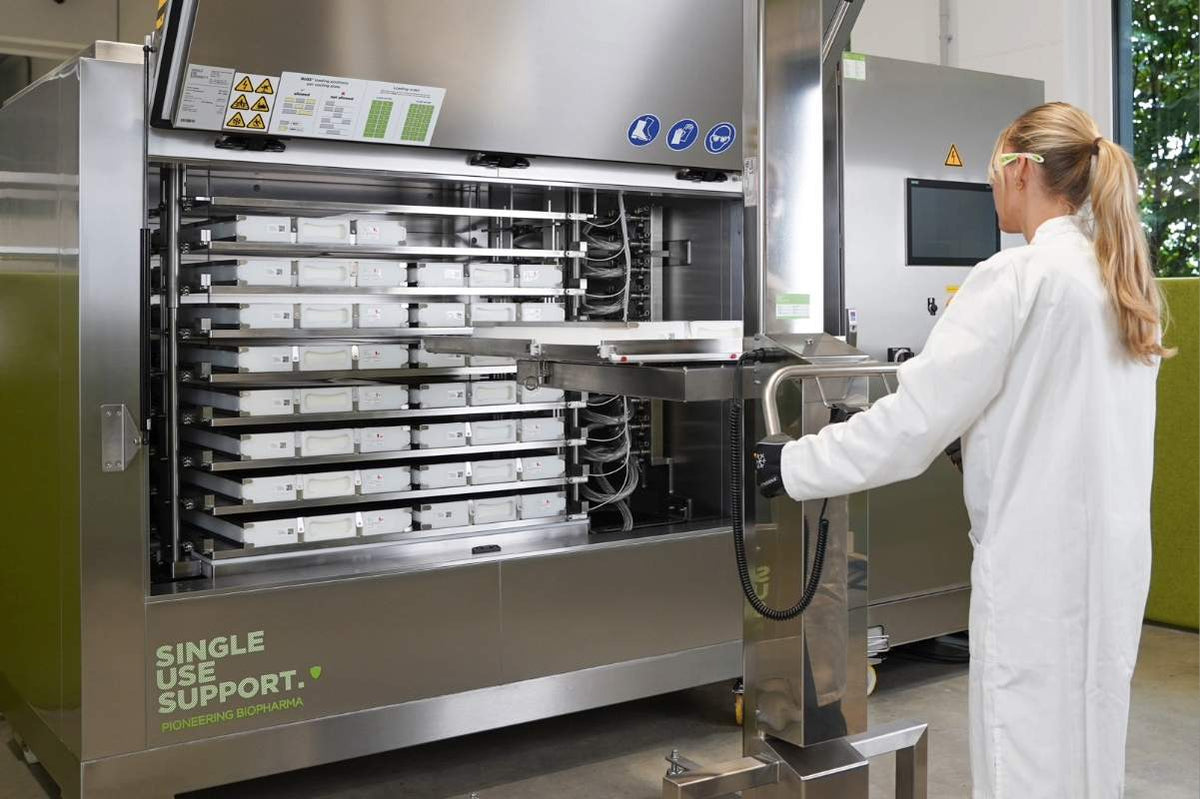 A woman in a white lab coat operates a large stainless steel single-use support freezing machine with multiple shells for single-use bags inside.