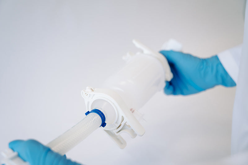 An image of a fluid transfer filter held by a person wearing blue gloves.