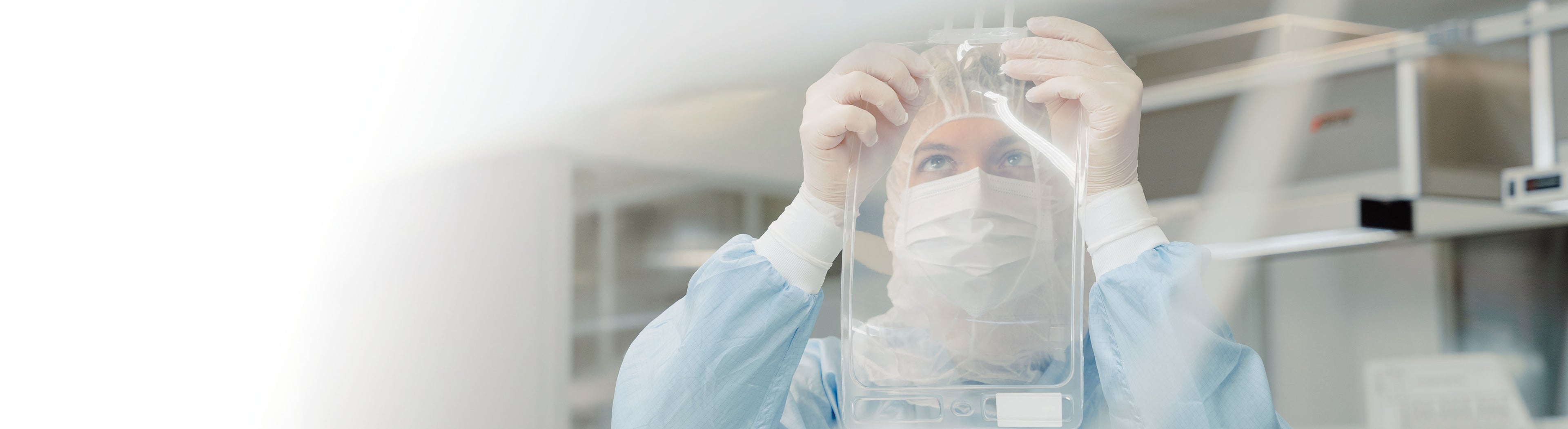 Person in a cleanroom suit and mask holding a clear single-use bag with a label in a laboratory setting